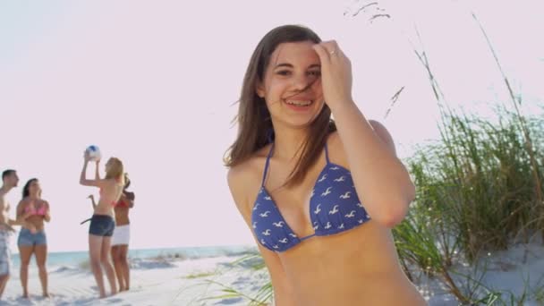 Chica sentada en la playa mientras sus amigos juegan pelota
 - Metraje, vídeo