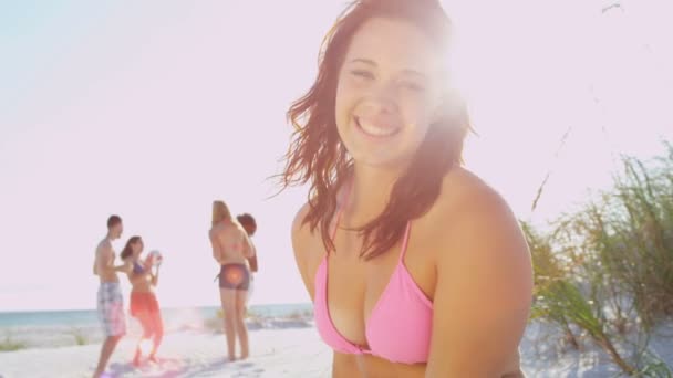 Chica sentada en la playa mientras sus amigos juegan pelota
 - Imágenes, Vídeo