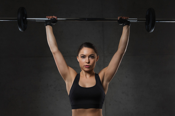 young woman flexing muscles with barbell in gym - Foto, Imagem