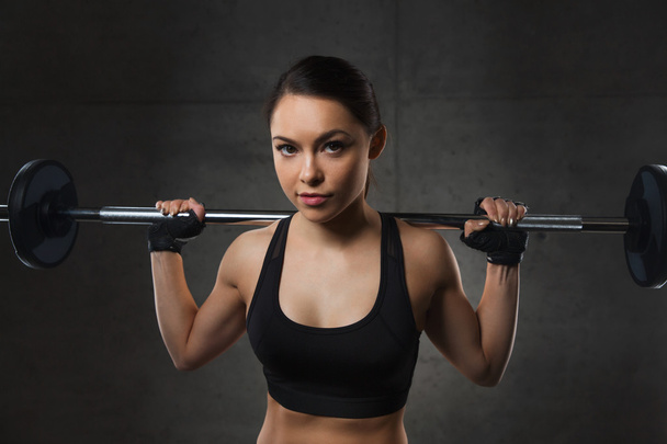 young woman flexing muscles with barbell in gym - Fotografie, Obrázek