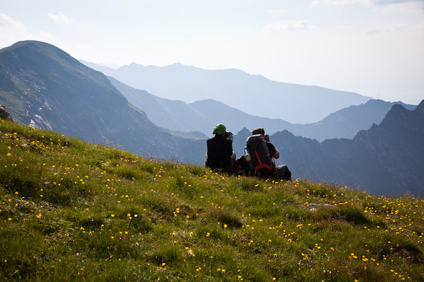Пара мандрівників захоплюється видом і фотографує високі гори
 - Фото, зображення