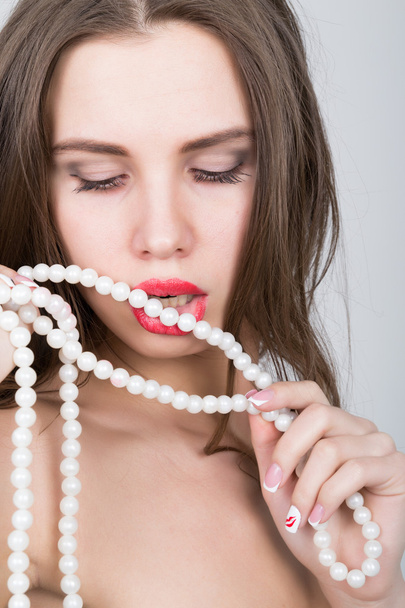 close-up portrait of a beautiful girl with red lips, holding a pearl necklace. mouth open, pearls touches her lips. Red Sexy Lips and Nails closeup - Foto, Imagem