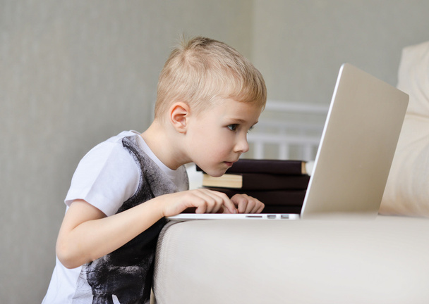 Маленький хлопчик сидить з ноутбуком на дивані вдома
 - Фото, зображення