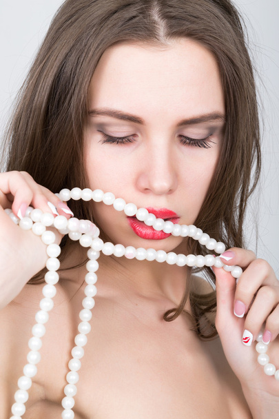 close-up portrait of a beautiful girl with red lips, holding a pearl necklace. mouth open, pearls touches her lips. Red Sexy Lips and Nails closeup - Zdjęcie, obraz