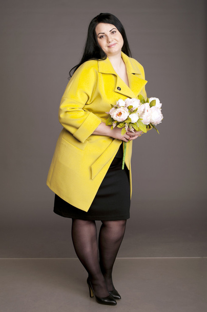 corpulent brunette in  in a yellow coat with a bouquet of flowers - Fotó, kép