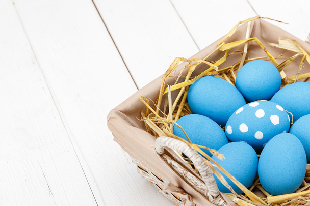 Blue easter eggs in a basket on a white wooden table - Фото, изображение
