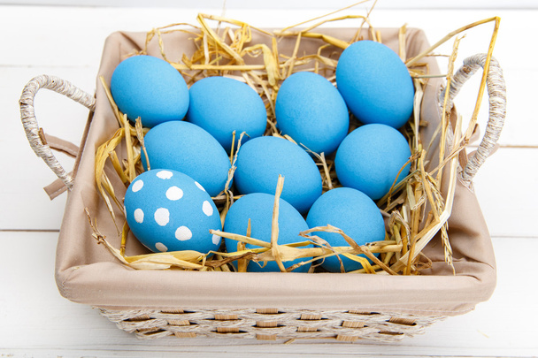 Blue easter eggs in a basket on a white wooden table - Fotó, kép