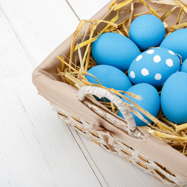 Ovos de Páscoa azuis em uma cesta em uma mesa de madeira branca
 - Foto, Imagem