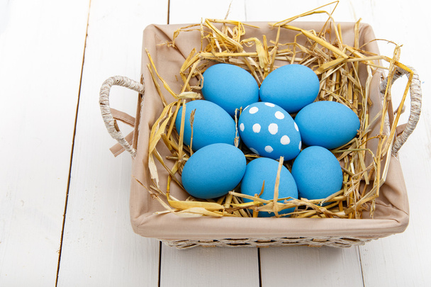 Blue easter eggs in a basket on a white wooden table - 写真・画像