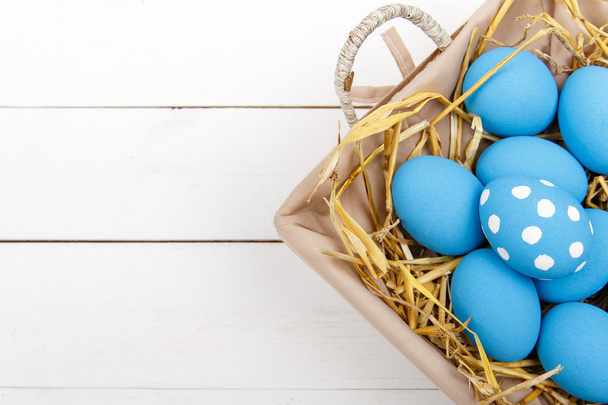 Oeufs de Pâques bleus dans un panier sur une table en bois blanc
 - Photo, image
