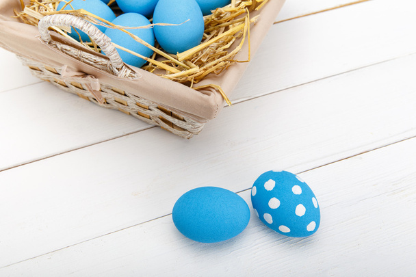 Blue easter eggs in a basket on a white wooden table - Zdjęcie, obraz