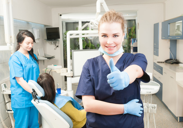 Pewny siebie, uśmiechając się kciuk kobieta dentysty się w jej gabinecie - Zdjęcie, obraz