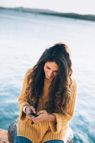 Young woman sitting on pier and chatting over phone - Photo, Image