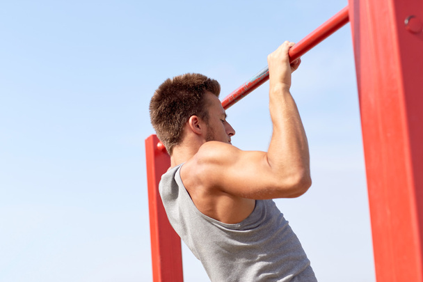 young man exercising on horizontal bar outdoors - 写真・画像