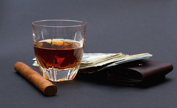 Glas Whiskey, Zigarre und eine Stange Geld auf einer braunen Brieftasche vor dunklem Hintergrund - Foto, Bild