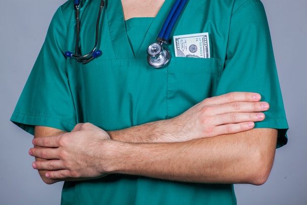 Doctors scrub top with stethoscope and one hundred dollar bill. - Foto, Imagen