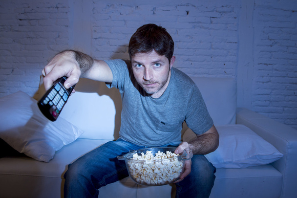 junger attraktiver Mann zu Hause auf Couch im Wohnzimmer vor dem Fernseher mit Fernbedienung liegend - Foto, Bild