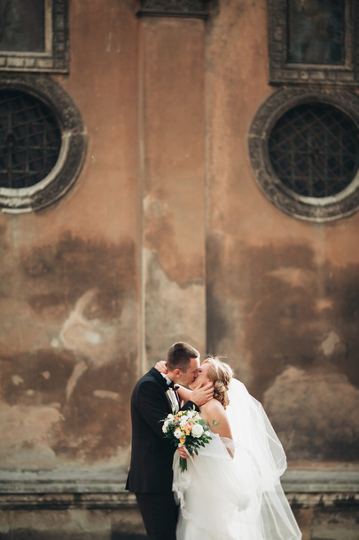 happy luxury wedding couple is standing and kissing in the streets of old city - Zdjęcie, obraz