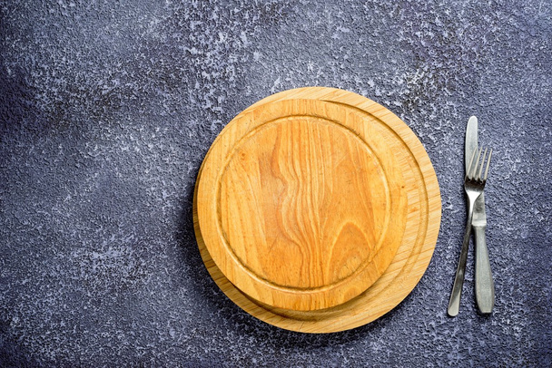 Dřevěný kulatý krájecí desky s prázdný prostor, vidlička a nůž na stůl. - Fotografie, Obrázek