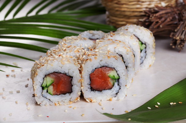 Roll with sesame sushi smoked salmon, cucumber, tropical leaves, still life food - Foto, imagen