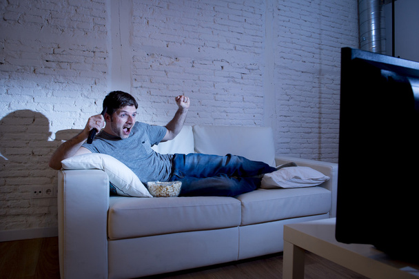  привабливий чоловік вдома лежить на дивані у вітальні дивитися спортивний матч на телебаченні святкування мети
 - Фото, зображення