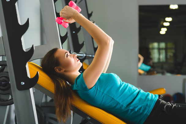 junge Frau trainiert mit Kurzhanteln im Fitnessstudio - Foto, Bild