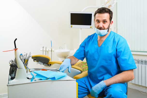 Portrait of happy male dentist wearing lab coat while sitting in clinic - Fotoğraf, Görsel