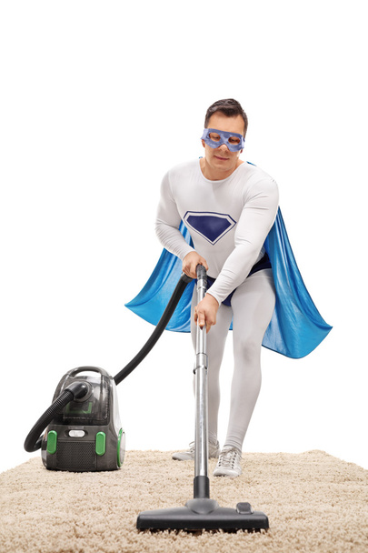 Man in a superhero costume vacuuming a carpet  - Foto, imagen
