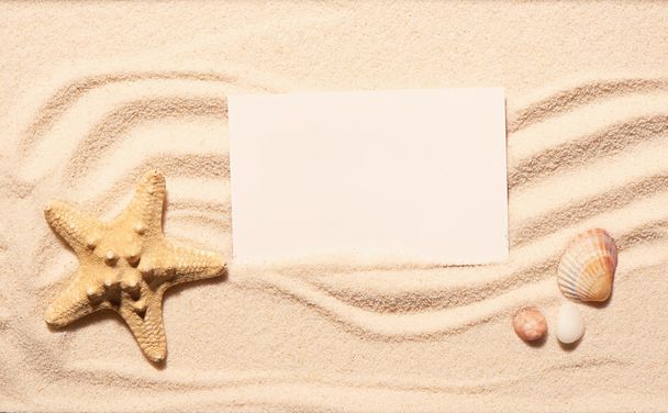Αστερίες, χτένι θαλασσινών κοχυλιών, πέτρες με λευκή κάρτα στην άμμο παραλία - Φωτογραφία, εικόνα