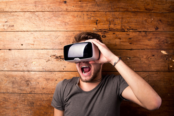 Man het dragen van Virtual reality bril. Studio schot, houten achtergrond - Foto, afbeelding