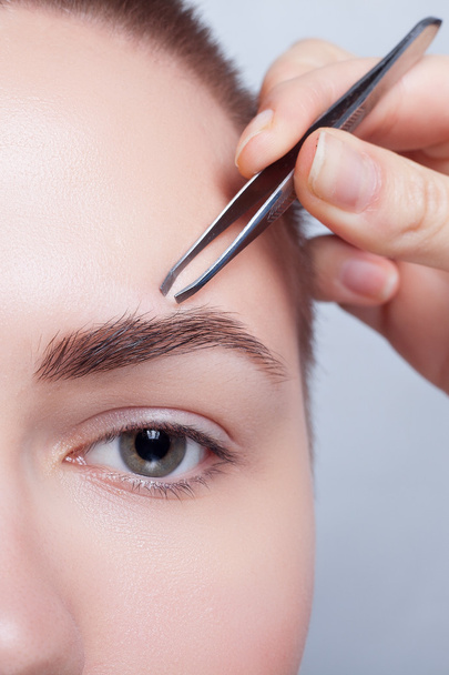 Young woman with short hair plucking eyebrows tweezers close up - Foto, Bild