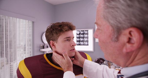 Senior medical doctor examining sports athlete's neck - Photo, Image