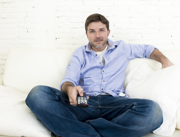 молодой счастливый человек смотрит телевизор, сидя дома гостиная диван выглядит расслабленной наслаждаясь телевизором
 - Фото, изображение