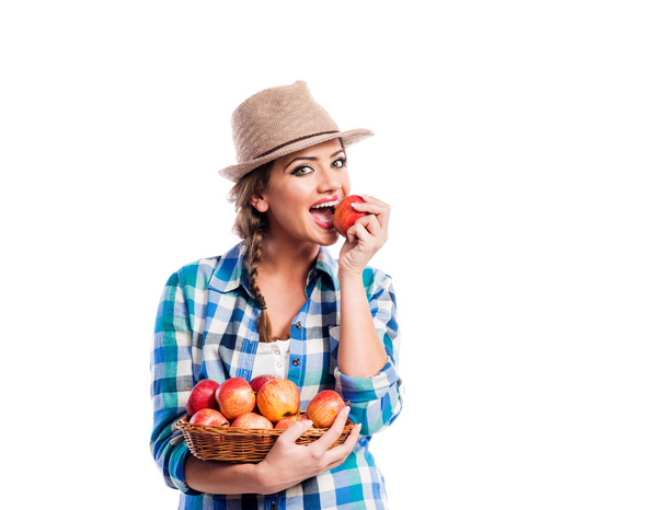Woman, checked shirt holding basket with fruit. Eating apple. - Fotoğraf, Görsel