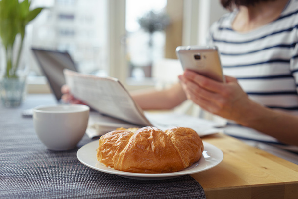 Женщина с сотовым телефоном завтракает круассаном
 - Фото, изображение