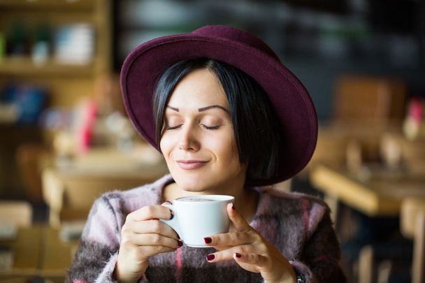 Girl in Cafe holding cup of hot coffee in hand, smiling - Фото, изображение