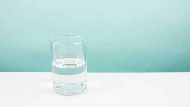 Half empty or half full glass of water on white table. - Foto, Imagen