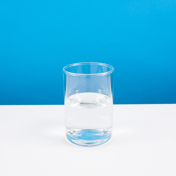空の半分または半分完全な白いテーブルの上に水のガラス. - 写真・画像