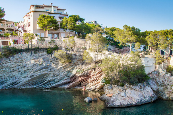 Luxusní Low Rise Mediterranean Resort Hotel nebo Dovolená Home Sedí na vrcholu skalnatého útesu s výhledem na tyrkysový rybník a obklopen zelenými stromy, osvětlené jasným sluncem během teplého západu slunce - Fotografie, Obrázek