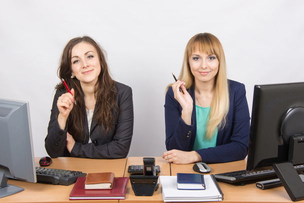 Dos mujeres de negocios sentadas en un escritorio, sosteniendo la pluma en la mano y mirando al marco
 - Foto, Imagen