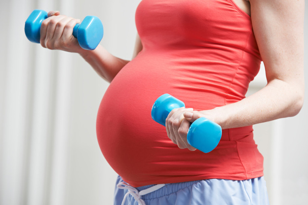 Крупним планом вагітна жінка вправляється з вагами
 - Фото, зображення