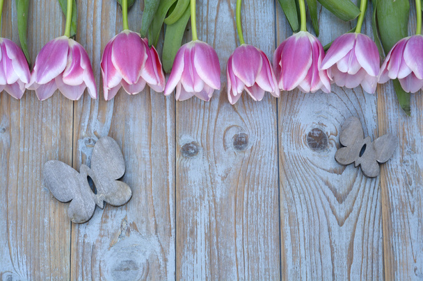 Old grey blue wooden background with pink white tulips border in a row  and empty copy space with wooden spring summer butterflies decoration - Photo, Image