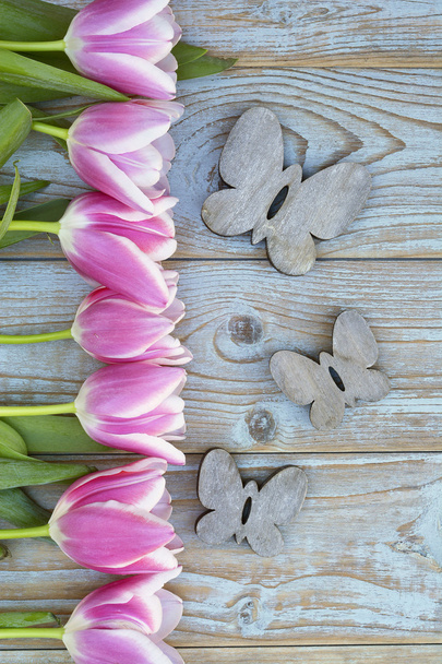 Vieux fond en bois gris bleu avec bordure de tulipes blanches roses dans une rangée et espace de copie vide avec décoration de papillons en bois printemps été
 - Photo, image