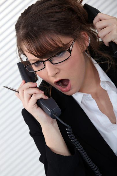 Stressed woman with two telephones - 写真・画像