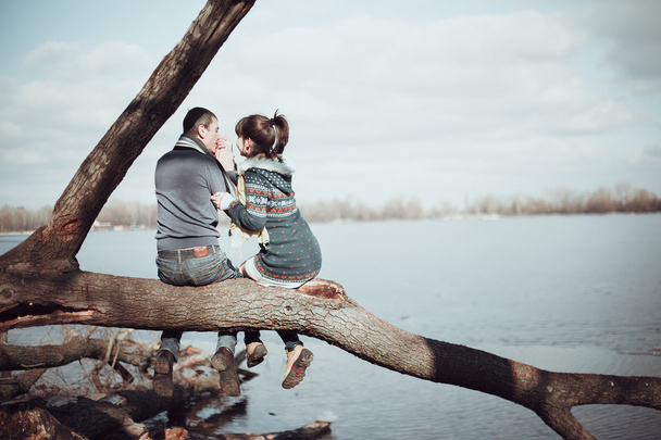 Romantic couple sitting on a branch near the water. - 写真・画像