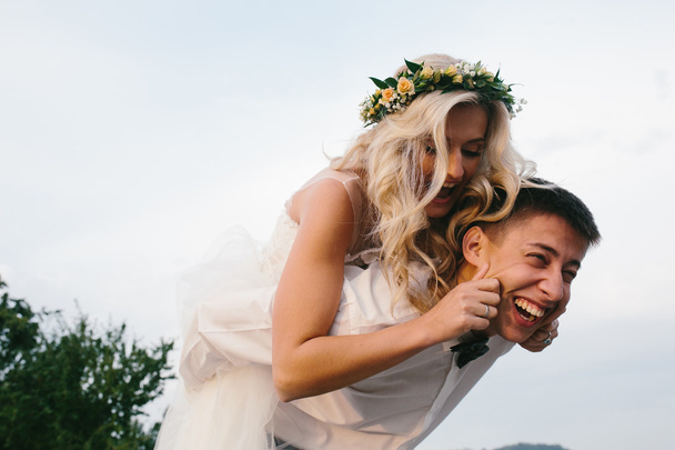 groom carries bride on his back outdoors - Photo, Image