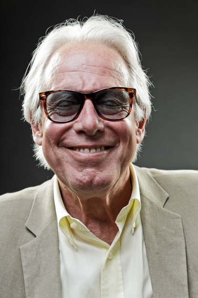 Smiling senior man in suit wearing sunglasses isolated on grey background. - Фото, изображение