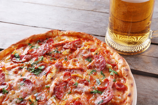 Tasty pizza and glass of beer are on wooden table, close up - Foto, afbeelding