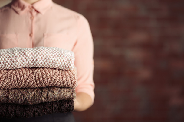 Stack of knitted clothes in female hands on blurred wall background - Valokuva, kuva