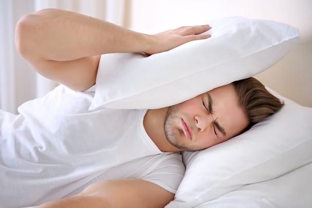 Young man with pillows lying in bed at home - Foto, imagen